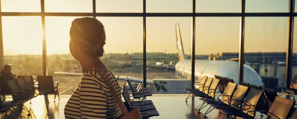 Woman standing in airport looking out at planes on tarmac